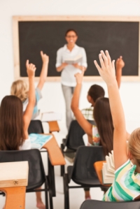 Little school children raising their hands in the classroom
